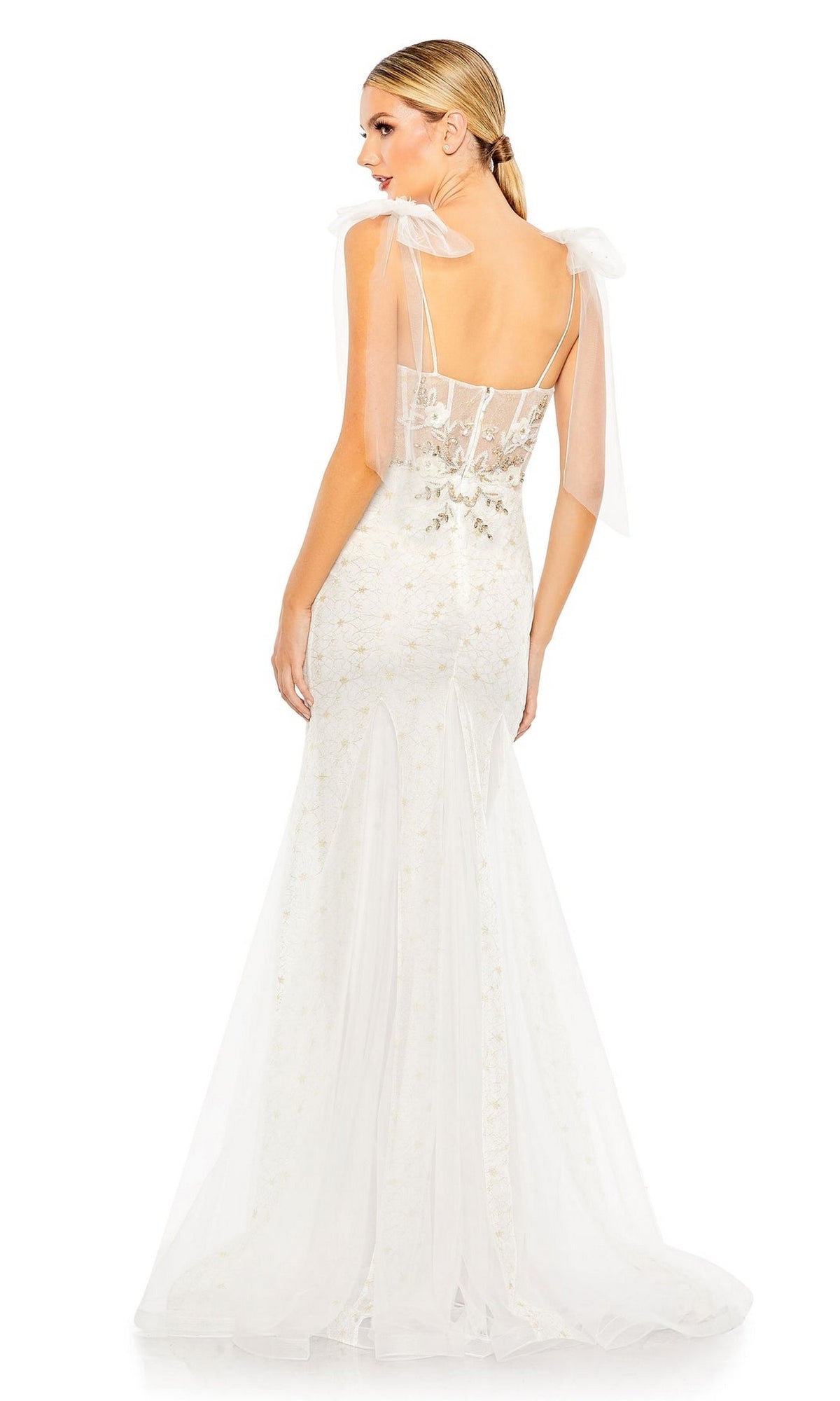 A woman stands facing away, showcasing the back and delicate details of the fitted white Long Formal Dress 50666 by Mac Duggal, featuring sheer straps and a flared mermaid skirt.